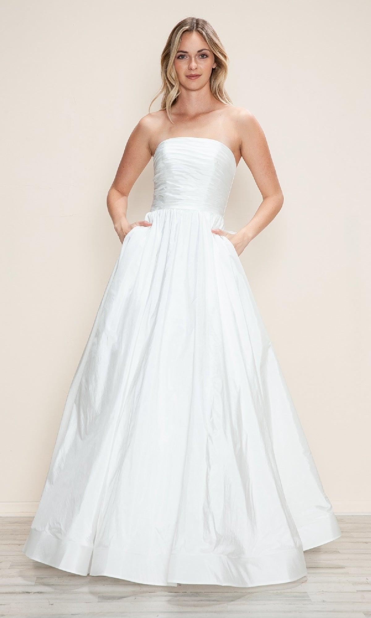 A woman poses against a plain light background, wearing the Poly USA 9754 long prom dress—strapless, floor-length white taffeta with side pockets and a ruched bodice.